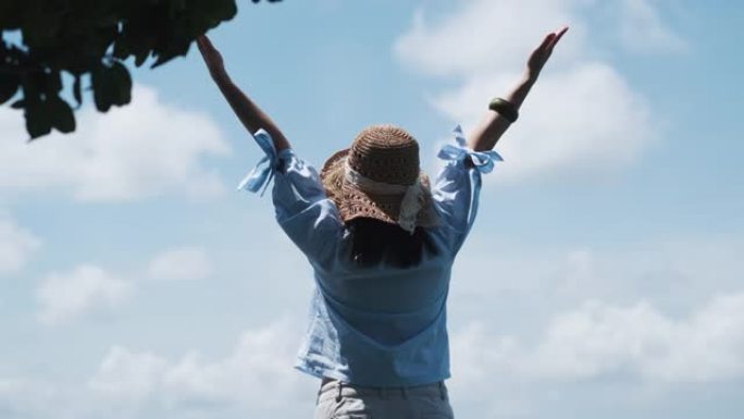 戴着帽子站在户外的女人旅行者的快乐肖像海滩海景女人举起手臂拥抱自然