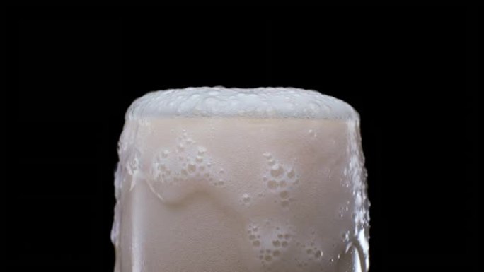 将带有气泡和泡沫的啤酒倒入黑色背景上的玻璃中，过度填充并用完，流过顶部。