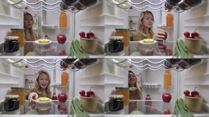 美丽的年轻女子打开冰箱门，向内看，开心地拿出蛋糕而不是苹果。从厨房冰箱里看。特写。慢动作准备59.9