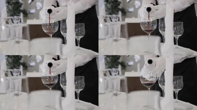 一个戴着白手套的服务员在餐馆里把红酒倒进杯子里的特写镜头。