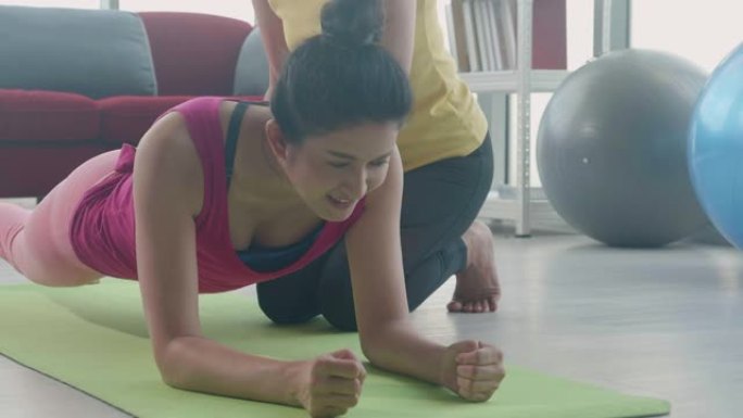 教练训练年轻的亚洲女性穿着运动服在健身中一起做铺板运动，女性用木板锻炼身体肌肉的强壮和力量，增加体重