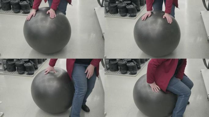 运动商店里的女人买了一个黑色的fitball。她坐在上面跳