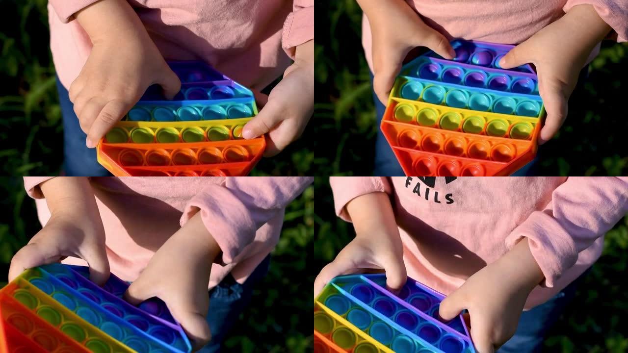 一个孩子带着流行的感官玩具在街上玩耍。女孩按下五颜六色的彩虹柔软的硅胶气泡。缓解压力和焦虑。时尚坐立