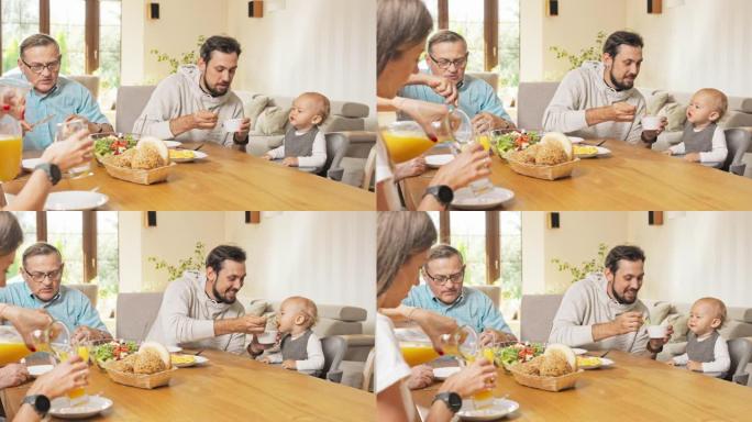 家庭早餐在餐桌上的家中，一个男人喂着坐在椅子上的小儿子，孩子食欲大增，旁边的一个女人将橙汁倒入玻璃杯