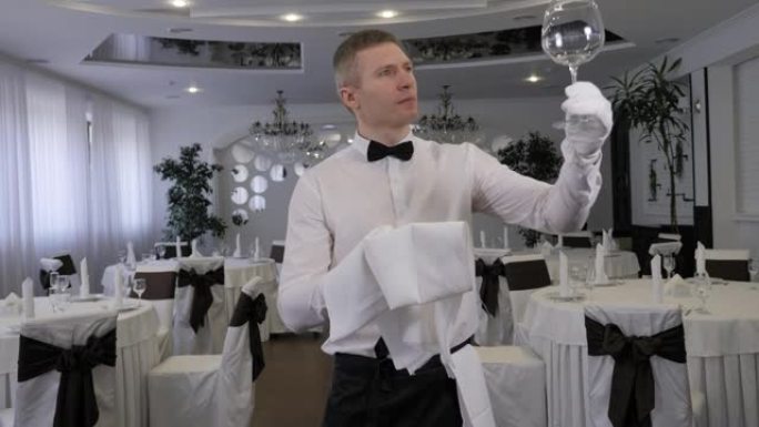 一个戴着白手套的服务员在餐厅用毛巾擦杯子。