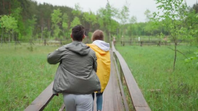 爱幸福的年轻夫妇在乡下享受时光。浪漫的徒步旅行者在雨中牵着手在林地的木路上奔跑