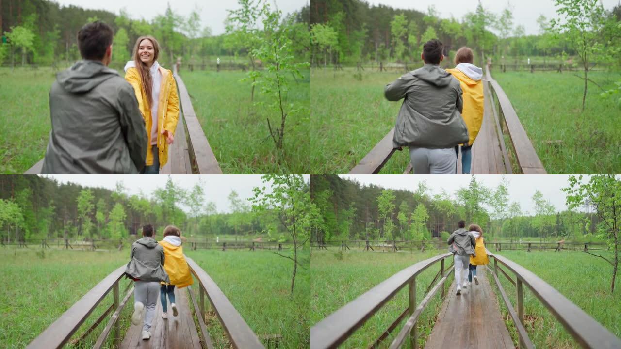 爱幸福的年轻夫妇在乡下享受时光。浪漫的徒步旅行者在雨中牵着手在林地的木路上奔跑