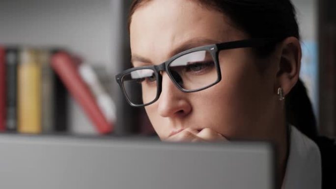 看着电脑屏幕的女人。戴着眼镜的忧心忡忡或沉思的女人的特写镜头，她不断地看着监视器屏幕