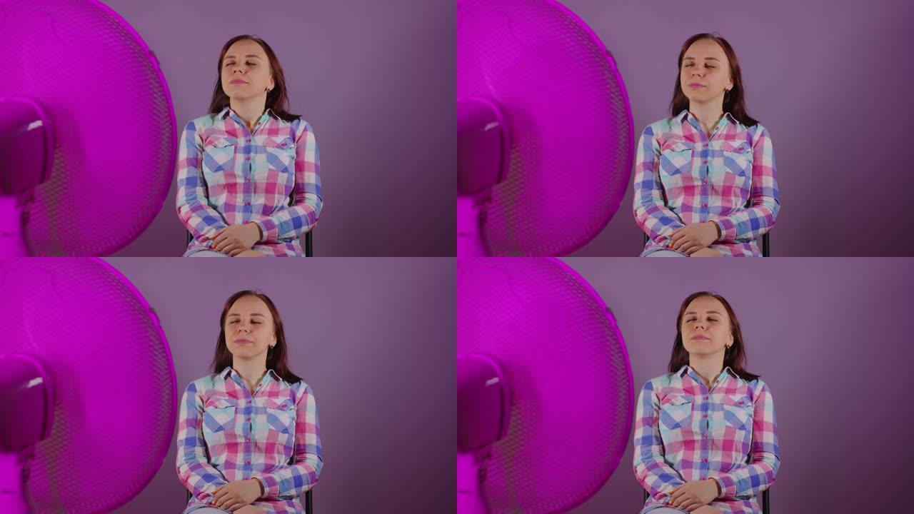年轻女子坐在紫色背景下的椅子上的特写镜头。快乐的黑发女人，闭着眼睛享受呼吸机的空气