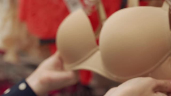 在百货公司内衣店选择胸罩杯尺寸的手的特写镜头。购物用女性内衣的概念