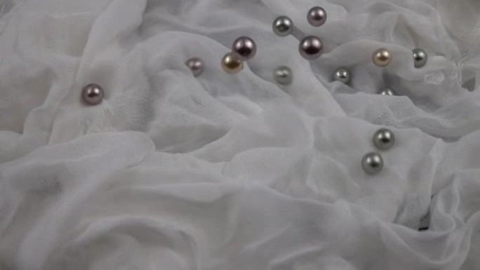 不同颜色的珍珠珠子落在白布上，慢动作