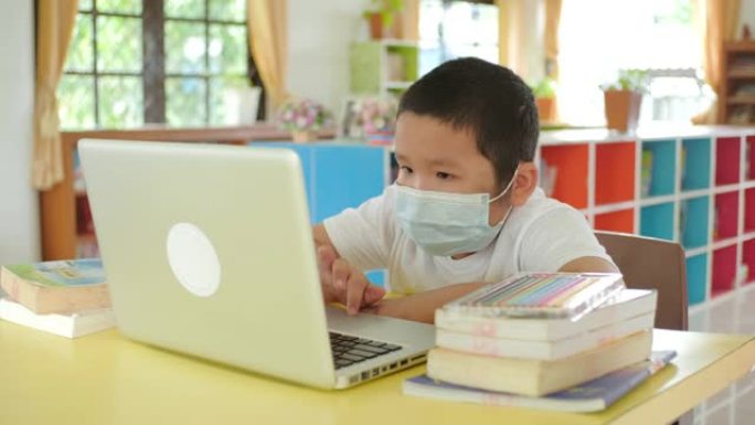 回到学校，在线学习，带口罩的亚洲小孩使用笔记本电脑进行在线学习。