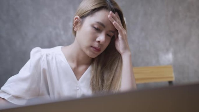 紧张不堪重负的年轻女商人穿着便装在电脑上工作，患有眼睛乏力或有痛苦的感觉，亚洲人职业倦怠综合症概念，