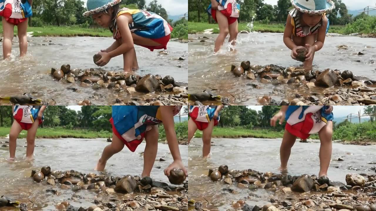 一个可爱的小女孩在乡村的溪流中放置一块岩石作为屏障。游戏，建水坝。童年幸福的概念。节水。