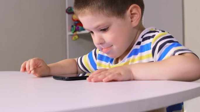 一个小男孩坐在桌子旁，按入手机屏幕。