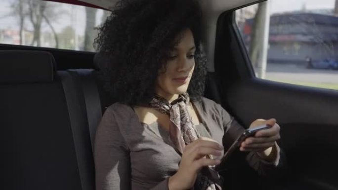时尚的年轻非洲裔美国妇女在智能手机上发短信的肖像。混血女性坐在后座的汽车上。特写。慢动作就绪59.9