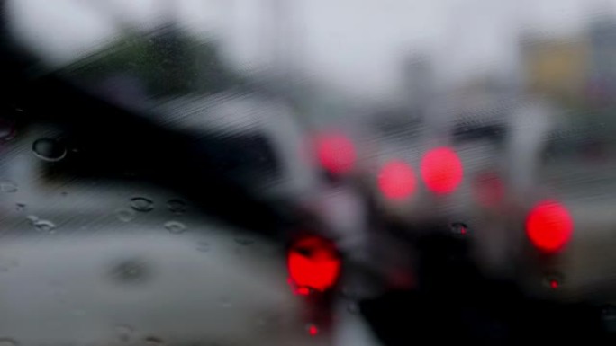 4k驾驶道路上的汽车停在挡风玻璃上的交通信号灯上，雨滴在挡风玻璃上。拍摄挡风玻璃。雨水落在汽车挡风玻