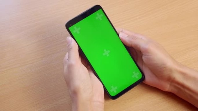 一个女人的手拿着手机，用手指在木桌的背景上用绿色屏幕翻页的特写镜头。chromakey。