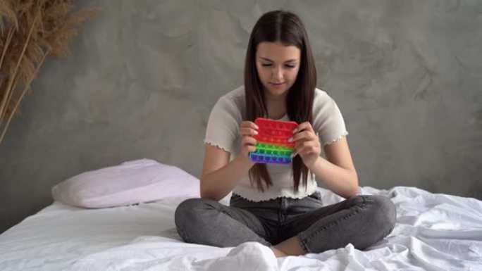 一个女人坐在床上的肖像和一个触摸玩具。lady stress将彩色彩虹柔软的硅胶气泡压在房屋墙壁的背
