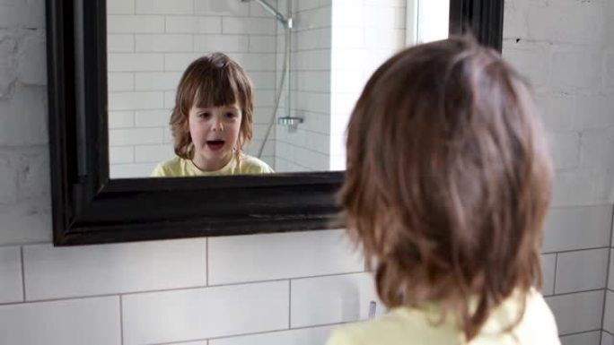 滑稽的长发学龄前儿童把脸拉进镜子里