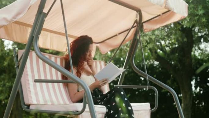 一个女人坐在秋千上的电影镜头在花园里看书