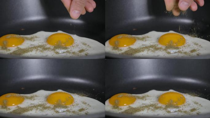 慢动作特写男人在煎锅上煮煎鸡蛋作为早餐，在家厨房。煎锅里的煎鸡蛋撒上磨碎的香料。手厨倒香料鸡蛋慢动作