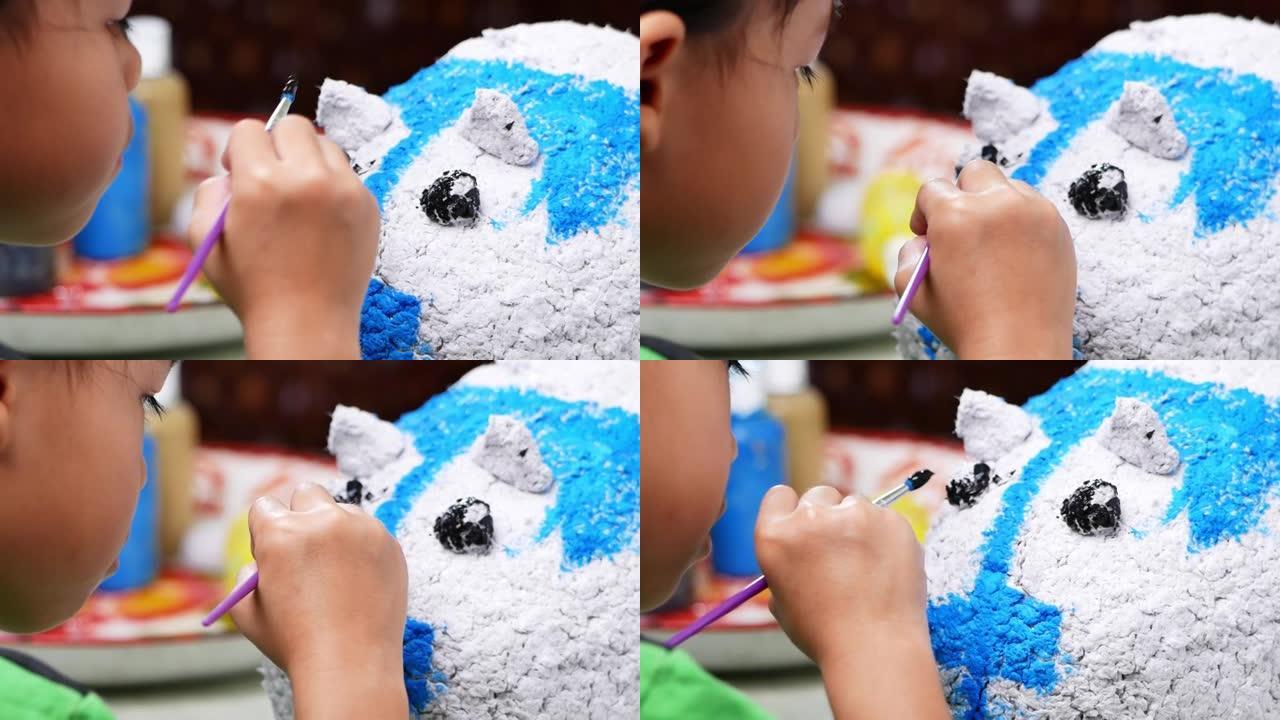 一个小女孩用刷子在家里一个白色的猪形纸浆的图形上画画。自己做存钱罐。