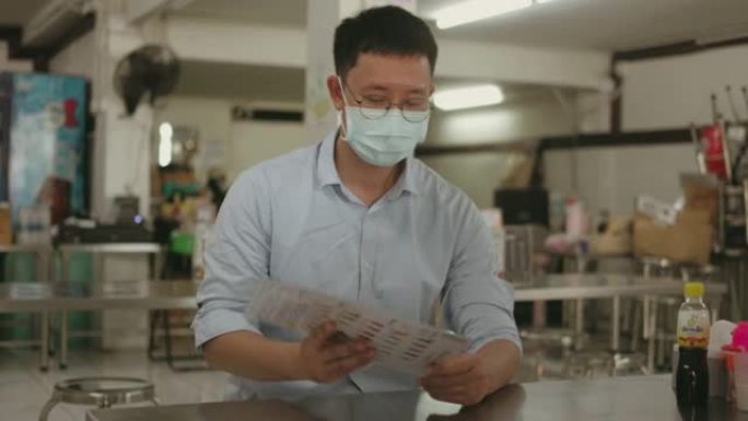 病毒流行期间，带防护面具的自由职业者翻转菜单在泰国当地快餐店选择餐饮-股票视频
