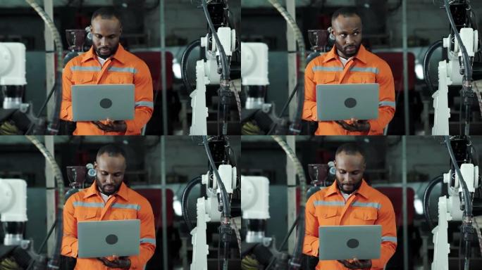 工程师非裔美国人使用计算机笔记本电脑来控制和编程制造业中的自动化机器人手臂机器。