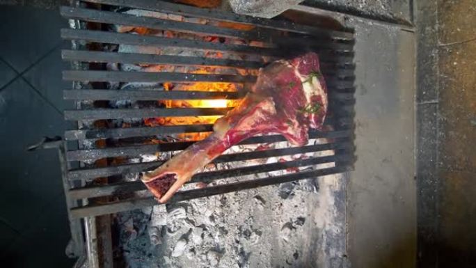 垂直视频。一位特写厨师将战斧牛排扔到火上。用煤在热烤架上烤一块多汁的牛排和香料和香草。高级美食餐厅。
