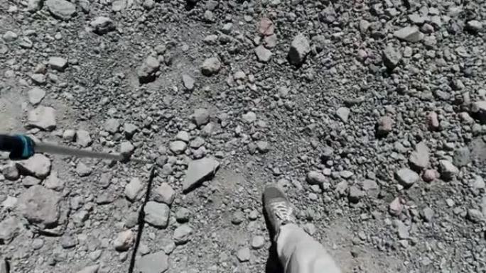 徒步旅行者的脚在山上的岩石下降中滑倒。夹。一名登山者用杆子向前行走的第一人称俯视图