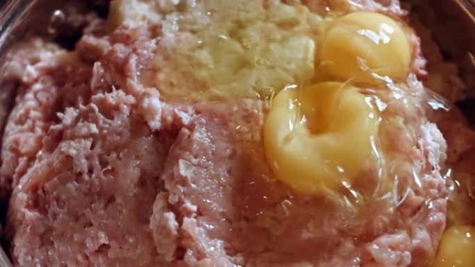 在金属碗中向新鲜碎肉中添加鸡蛋的特写镜头。在家做午餐。肉排的制备工艺