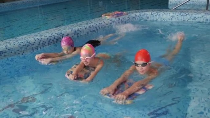 一群戴着游泳帽的孩子在室内游泳池的游泳课上。
