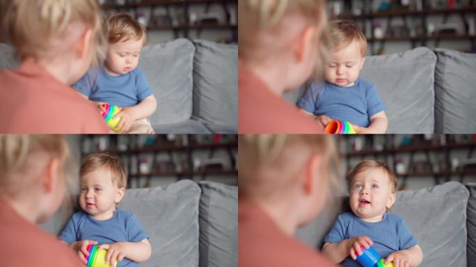 放大小女孩和男婴哥哥聊天，玩一堆坐在沙发上的彩色塑料杯。关爱蹒跚学步的弟弟的妹妹