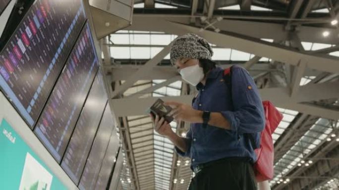 带保护面具的年轻亚洲男性在机场检查登机牌和到达离境板-股票视频