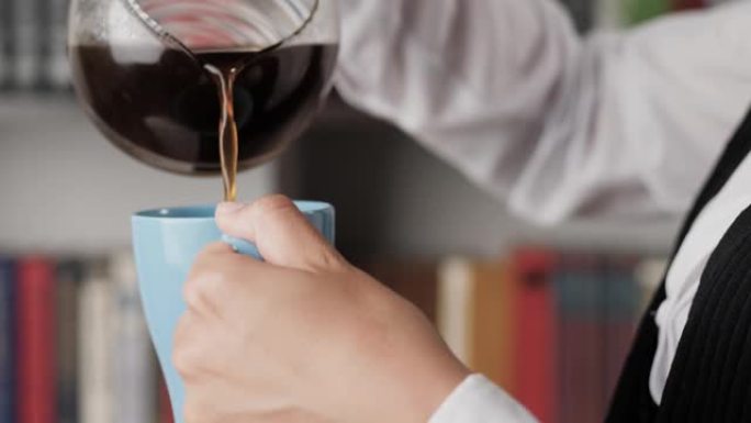 女人倒咖啡。女性手的侧视图将咖啡从咖啡机倒入蓝色杯子。特写