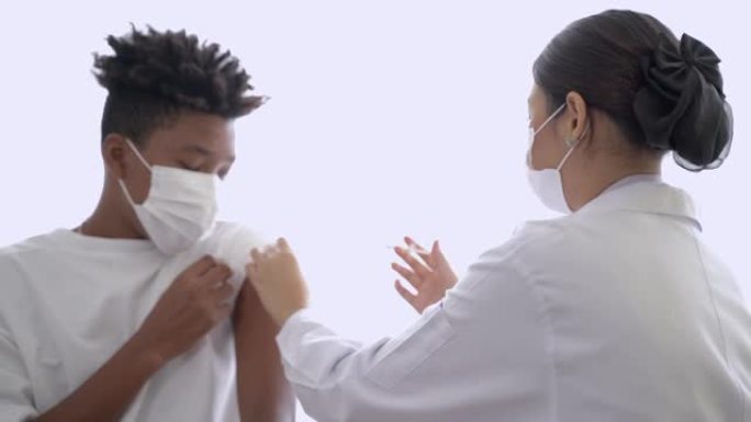 女医生使用注射器从瓶子里取疫苗注射给非裔美国男子以获得免疫力，以保护病毒。戴着防护面具的少年。