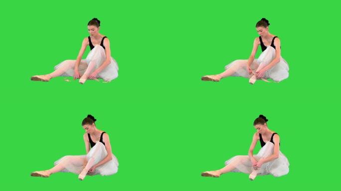 芭蕾舞女演员坐在绿色屏幕上的地板上，用芭蕾舞丝带将脚尖系起来，色度键