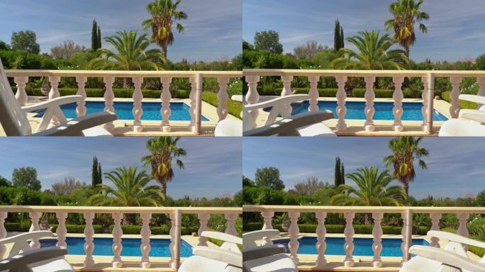 摄像机从左到右，向侧面移动，露台的石柱，别墅的阳台，俯瞰美丽的游泳池。供游客参观的有棕榈树的花园。