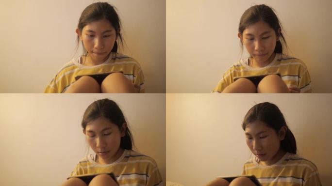 亚洲女孩在夜间通过智能手机在床上观看电影或病毒视频，并带有温暖的光线，生活方式的概念。