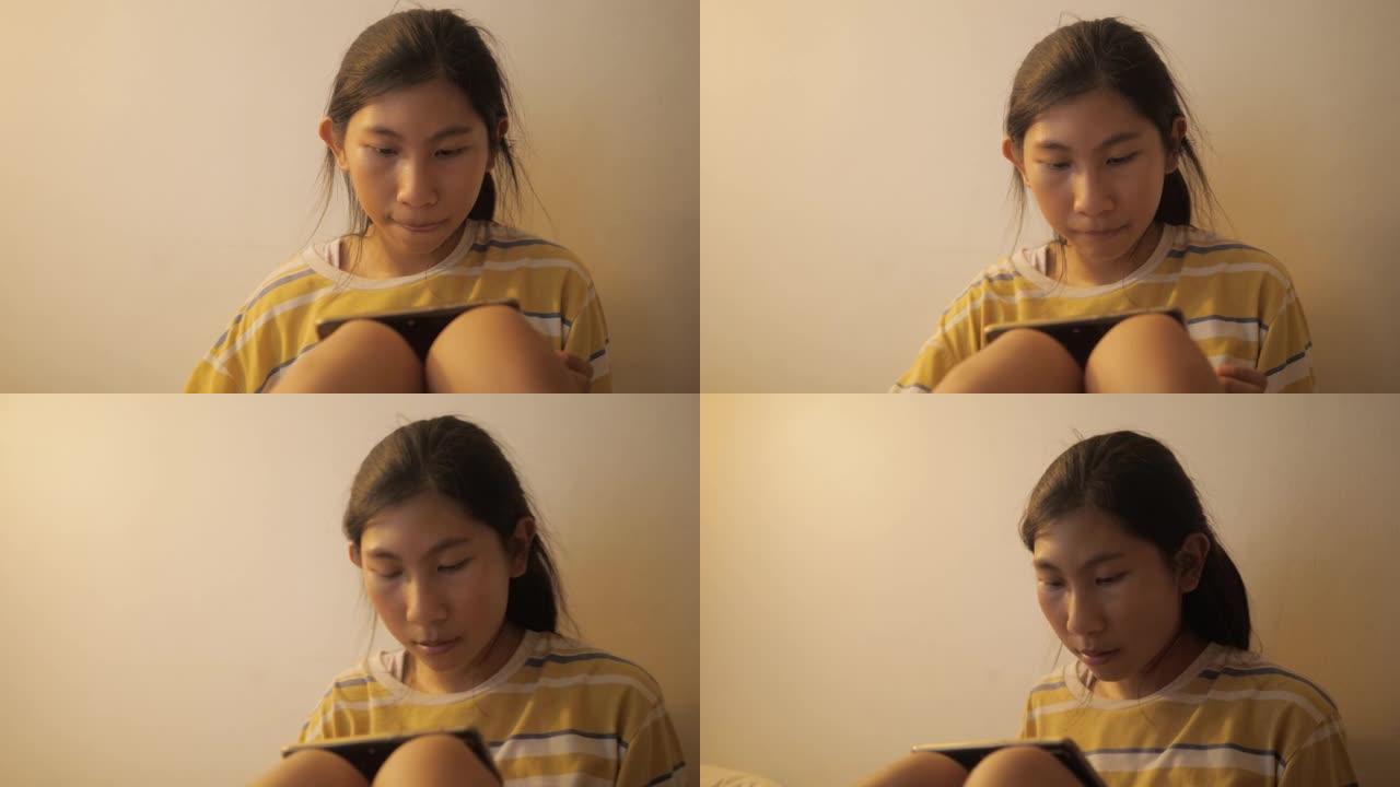 亚洲女孩在夜间通过智能手机在床上观看电影或病毒视频，并带有温暖的光线，生活方式的概念。