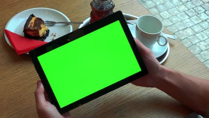 一名男子在智能手机上方的桌子上方拿着带有绿色屏幕的平板电脑，上面是进餐的特写镜头