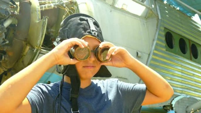 男孩在一架被毁的老式飞机附近，戴着老式飞行员的头盔和飞行护目镜
