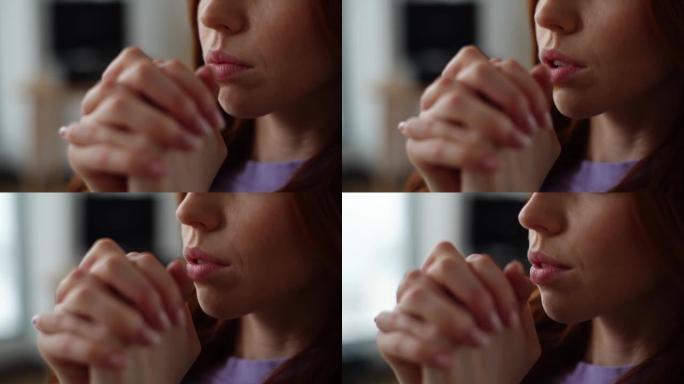 绝望的年轻女子的极端特写镜头，闭着眼睛真诚地祈祷，双手交叉在家里的脸前。