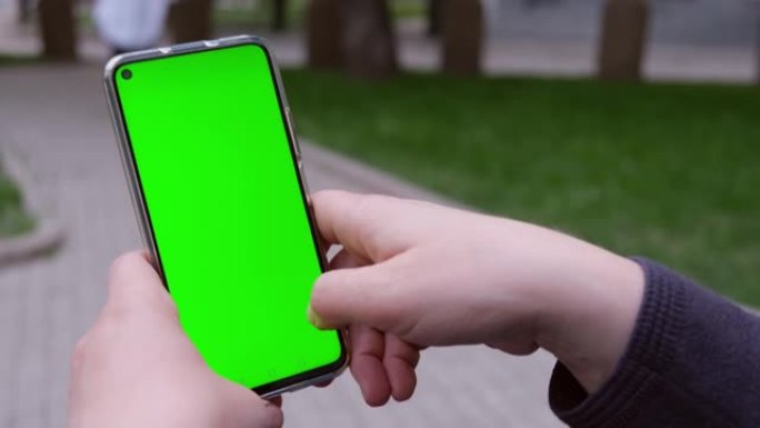 女人在街上坐在长凳上，使用带有绿色模拟屏幕色度键的电话。