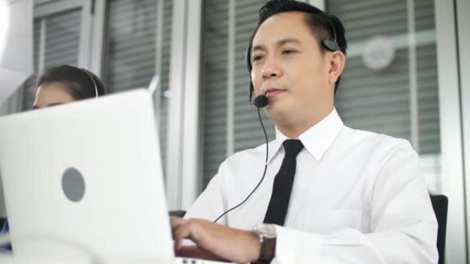 亚洲男性呼叫中心通过佩戴耳机和支持客户来工作