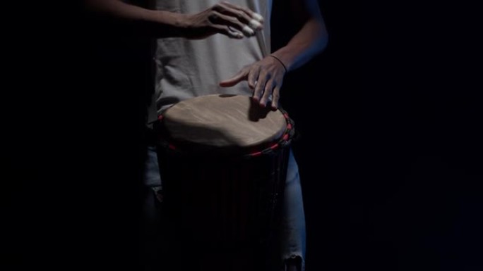 黑人鼓手在黑暗中在工作室里用手演奏非洲鼓。黑人音乐家用手击鼓