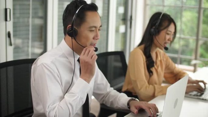 亚洲男性呼叫中心通过佩戴耳机和支持客户来工作