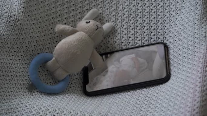 手机上的视频婴儿监视器应用程序在婴儿睡在婴儿床的智能手机屏幕上实时监控
