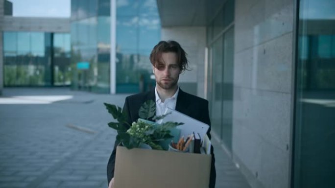 沮丧的被解雇的男雇主带着一盒个人物品走出办公楼的户外肖像
